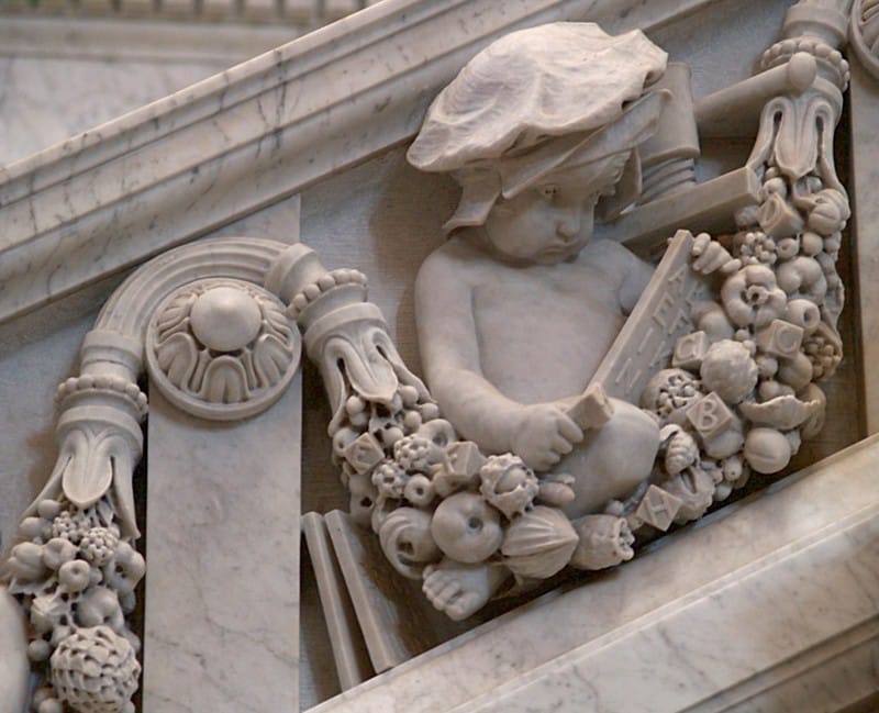 A marble sculpture of a child under an early printing press, and over a cornocupia that (unusually) has not only fruits but also letter blocks.